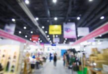 Booth Setup Tips for Your First Comic Book Convention A blurry view of a convention center, complete with signs and booths for fans and artists to sell their creations.