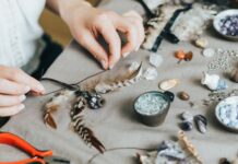 How To Make Custom Jewelry for Your Cosplay A person ties up a string to create a customized feather jewelry. On the table are multiple gemstones and rocks.