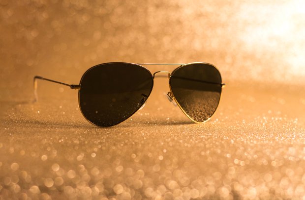 Most Famous Aviator Sunglasses in Movies A pair of aviator sunglasses resting against a golden background with dots of light reflecting off the lenses.