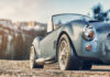 4 Muscle Cars Made Famous by Hollywood Movies A gray convertible classic car with chrome details and round headlights parked in front of snowy mountains.