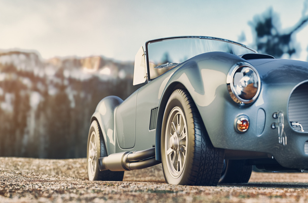 A gray convertible classic car with chrome details and round headlights parked in front of snowy mountains.