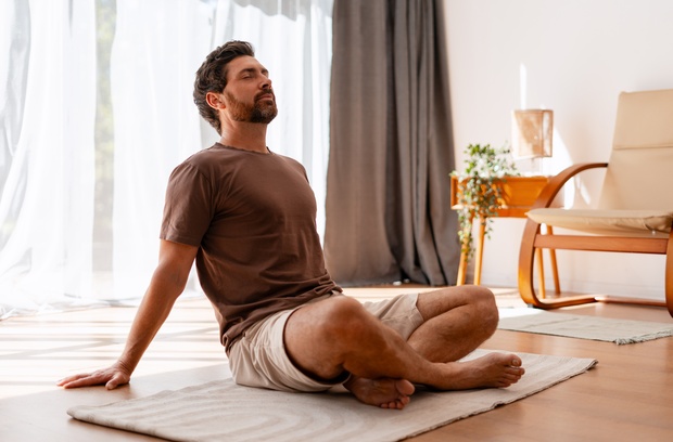 5 Interesting Hobbies That Will Make You Feel Like Batman A man sits on the floor of his home, practicing meditation with his eyes closed. He wears a brown shirt.